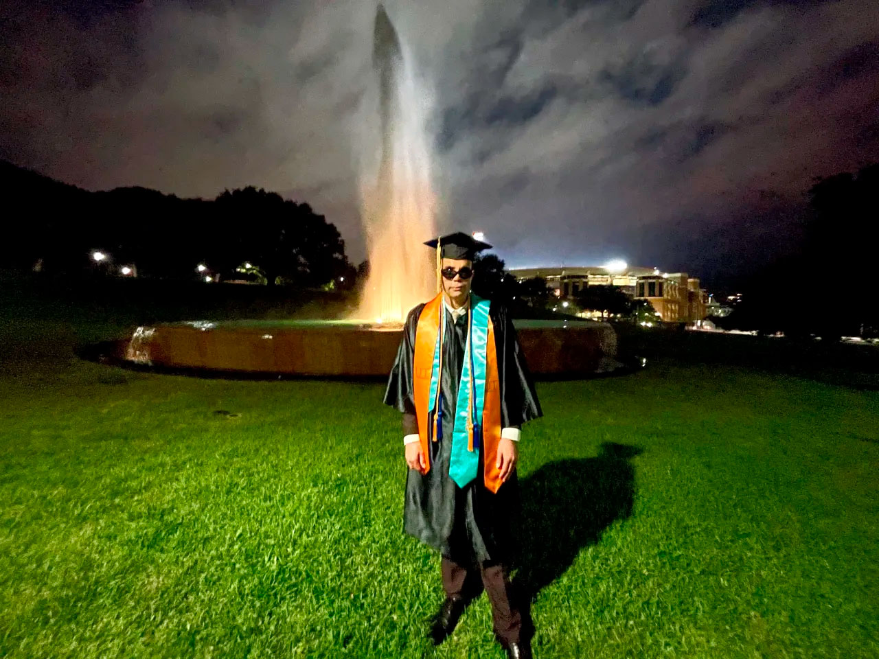 Qusay in graduation gown and cap by fountain